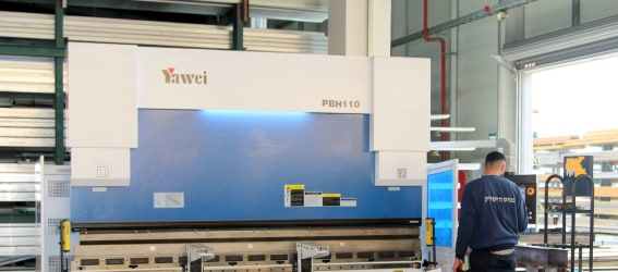 מכונה כחולה גדולה עם הכיתוב "YAWEI PBH110", משמשת לכיפוף מתכות בתעשייה. עובד נראה עובד על המכונה בסביבת עבודה תעשייתית.