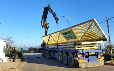 שער ברזל צהוב מונח על משאית הובלה עם מנוף במהלך פריקה או התקנה.