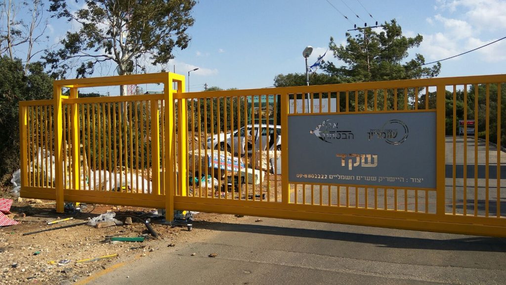 שער קונזולי צהוב ממתכת במילוי פרופילים מרובעים בצהוב ולוח במרכזו עם חריטת לייזר של הכיתוב "שקד"