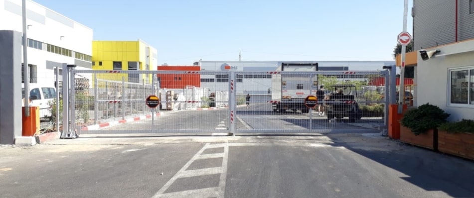 שער מתכת גדול בצבע כסוף המוצב בכניסה למתחם תעשייתי, עם דלת כפולה פתוחה חלקית