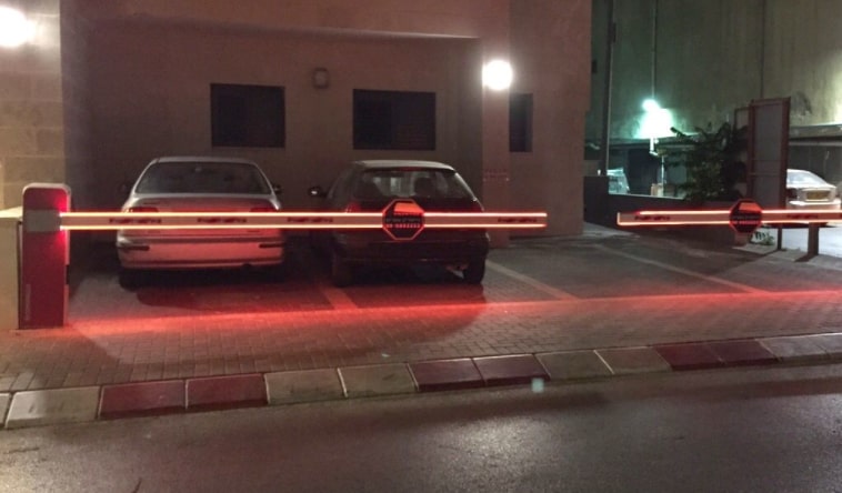 מחסומי זרוע בצבע אדום לבן מוארים בלילה חוסמים חניה פרטים ועם תמרורים מתומנים על גביהם
