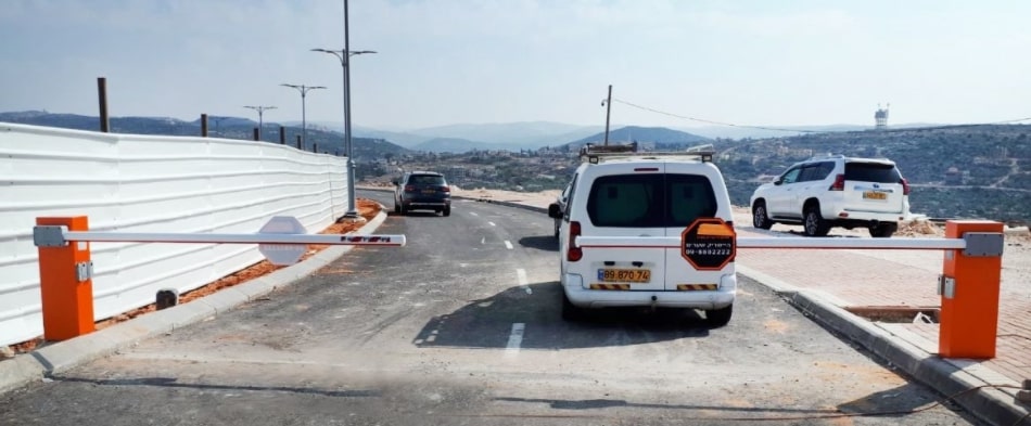 מחסומי זרוע חשמליים בצבע כתום ולבן החוסמים כביש וניתן לראות סביבה הררית ורכבים ברקע