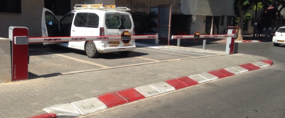מחסומי חניה חשמליים בצבע אדום ולבן חוסמים חניה פרטית וניתן לראות ברקע רכב לבן