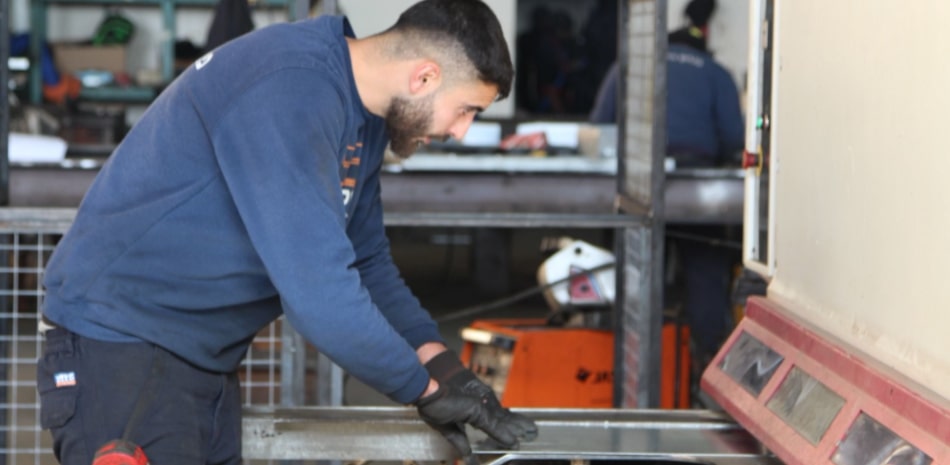 תמונה של עובד המתעסק במכונת חיתוך ומניח את ידיו על פחי מתכת שטוחים בצבע כסוף
